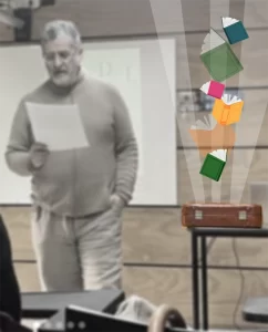 Carlos Lloró leyendo con su maletín a un costado, del cual salen libros multicolores